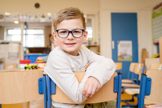 Jongetje met bril zittend op stoel in lege klas
